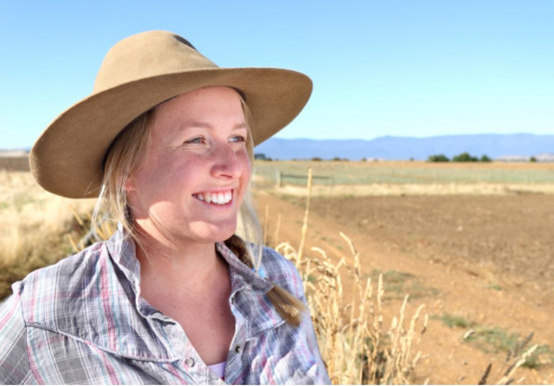 A woman wearing a hat looking out at paddocks.
