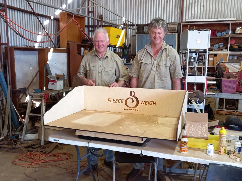 Two men in a shed standing behind a large set of scales for weiging fleeces.