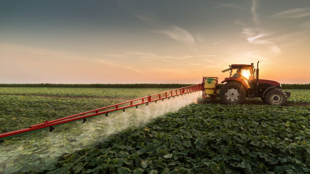 Side profile of a tractor dragging a pesticide rig to spray their crops