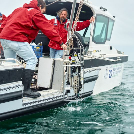 Men on a boat with scientific equipment hanging over the side on a winch.
