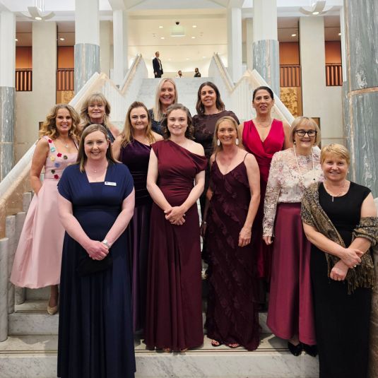 A group of 11 formally-dressed women standing on a staircase.
